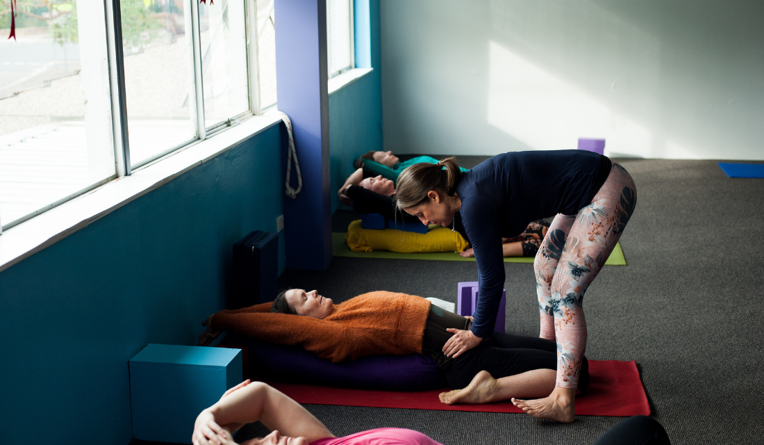 An image of three people doing yoga with one instructor assisting one of the participants.