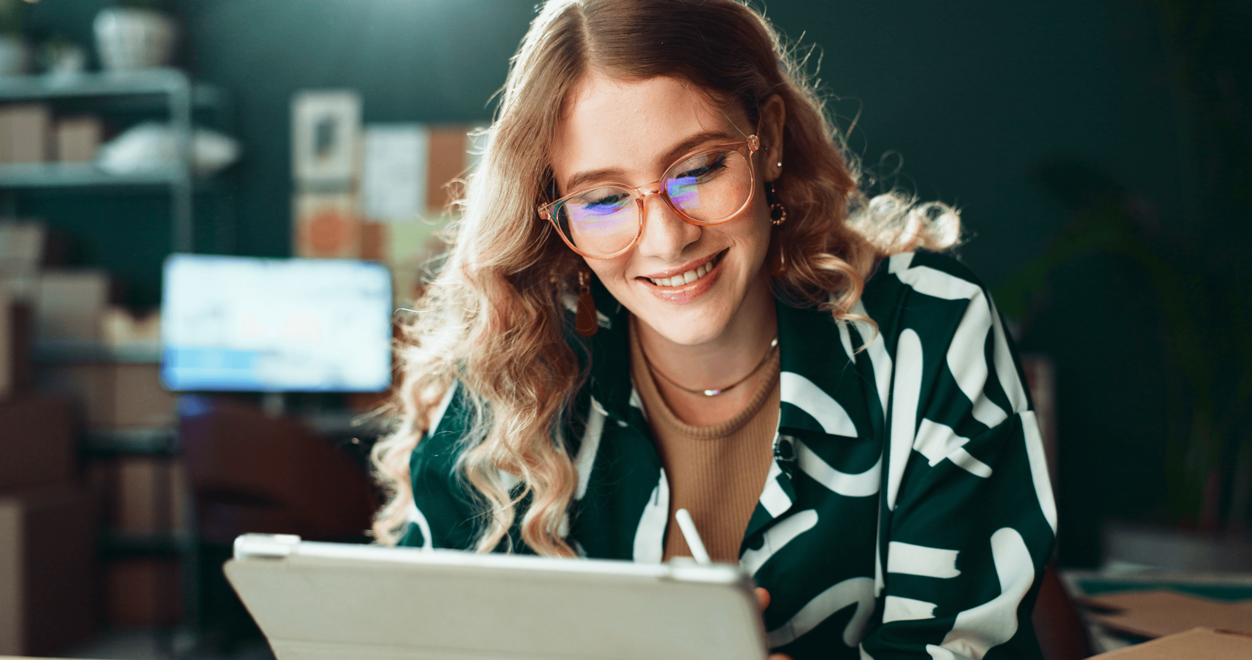 A woman wearing glasses and smiling, while working at her laptop.