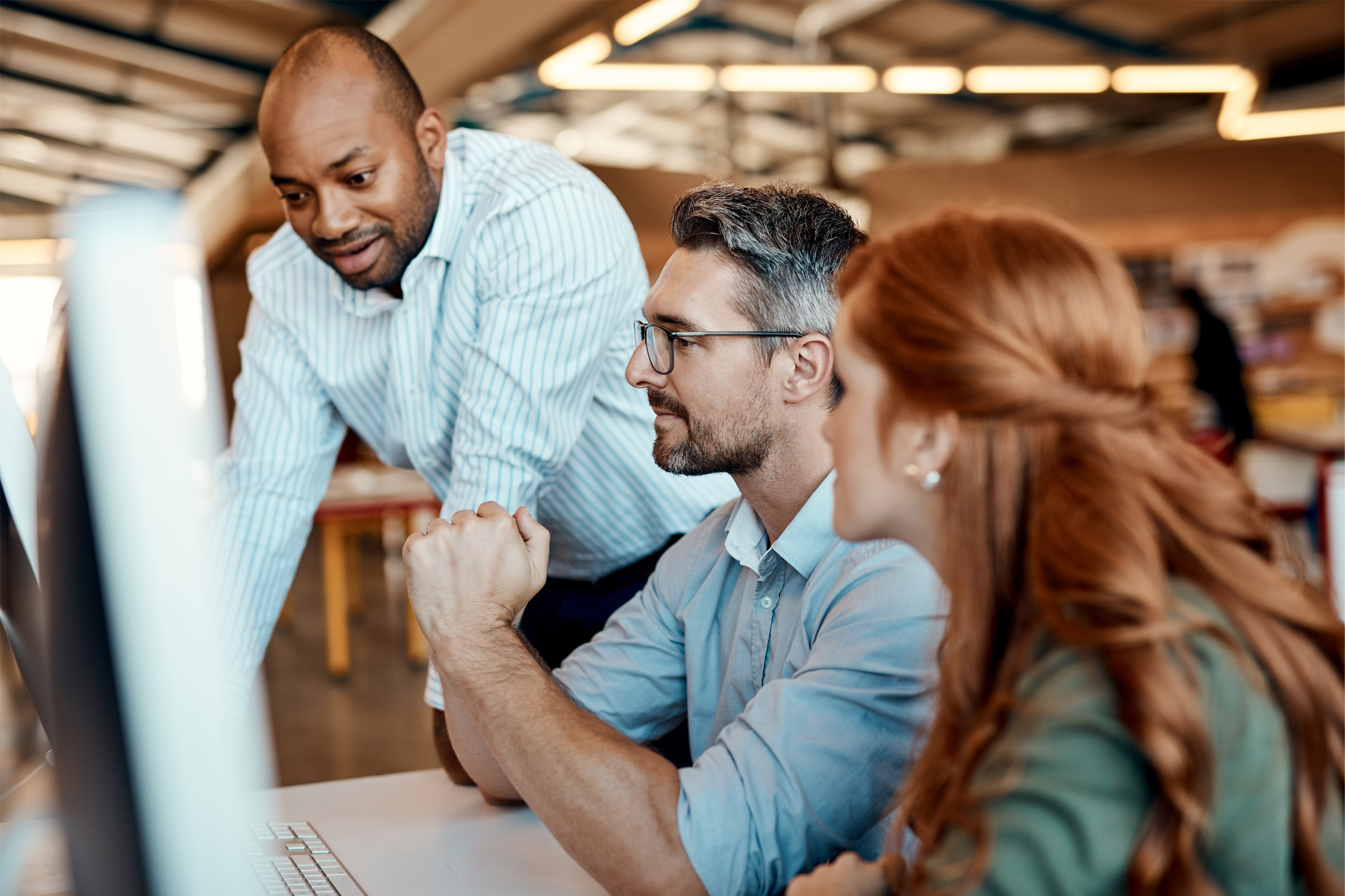 Three office workers, sat around a desk in discussion.