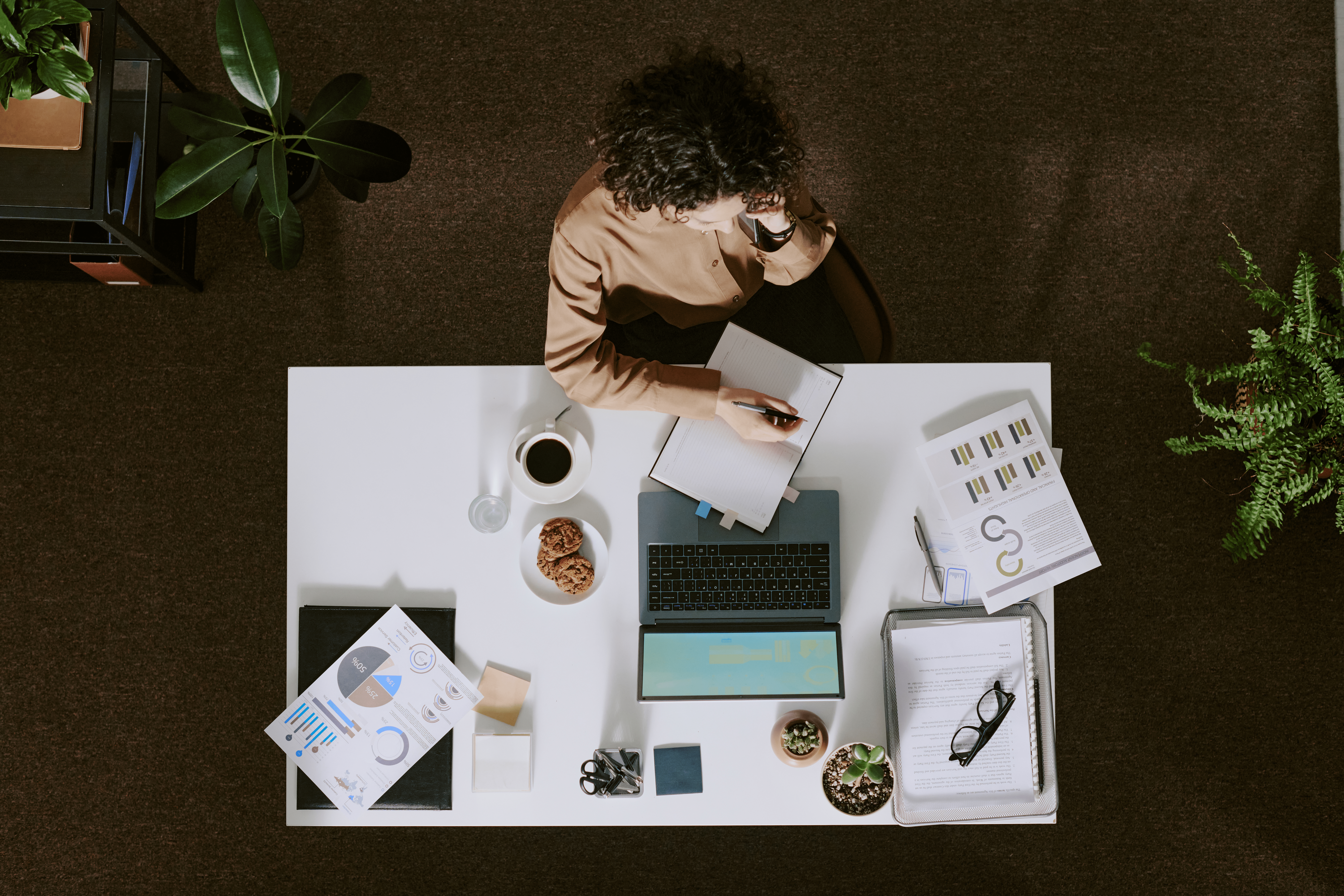 An ariel shot of a woman working at a desk, surrounded by paperwork and a laptop.