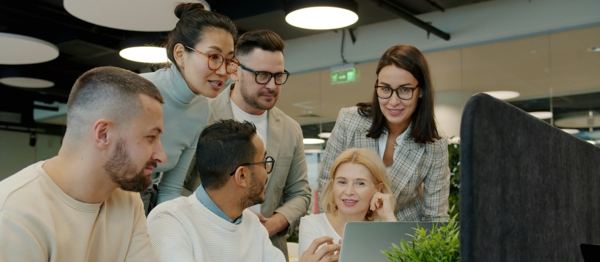A group gathered around a laptop screen, smiling and discussing.