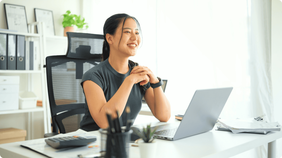 A woman working on her laptop on a tidy desk, smiling.